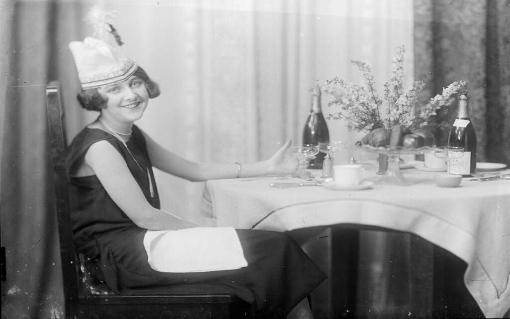 Three-quarter-length portrait of lady, to left, smiling and sitting on chair at table