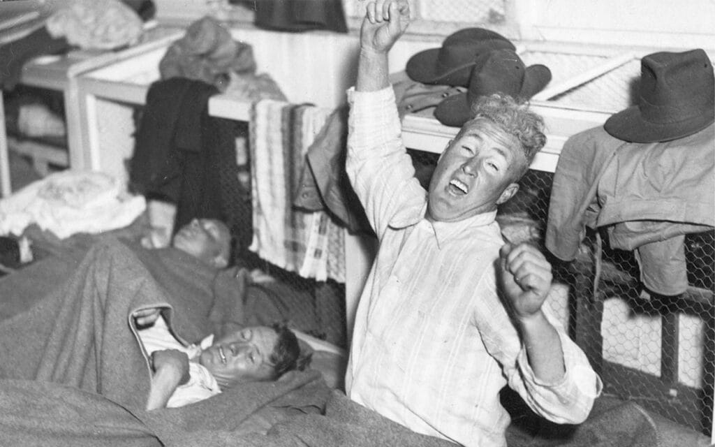 Shows a soldier stretching before getting out of bed and others in bed just waking up.