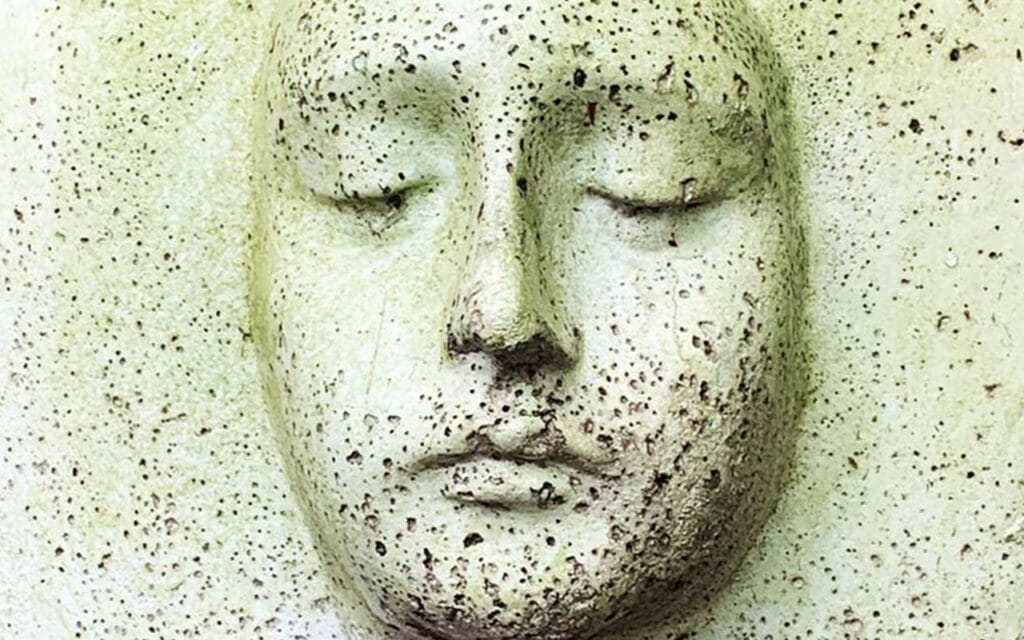 Close up of a concrete plant pot featuring a face looking downwards.