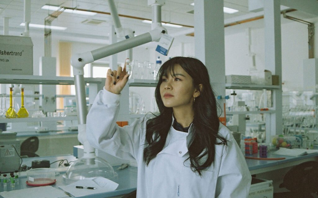 A woman wearing a white coat holding a vial of liquid in the air