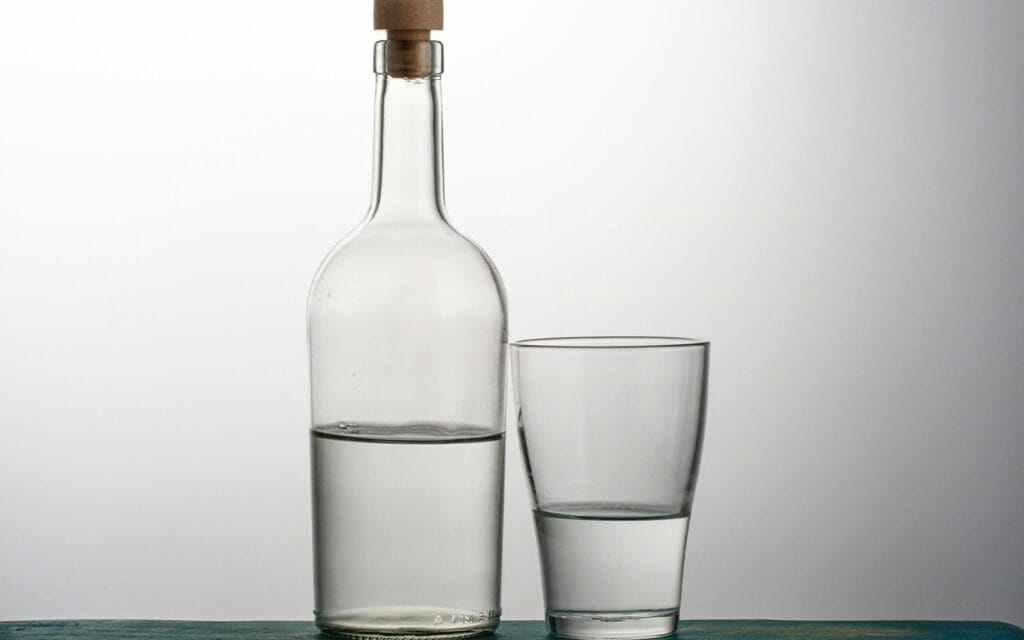 a half glass of water next to a half bottle of water