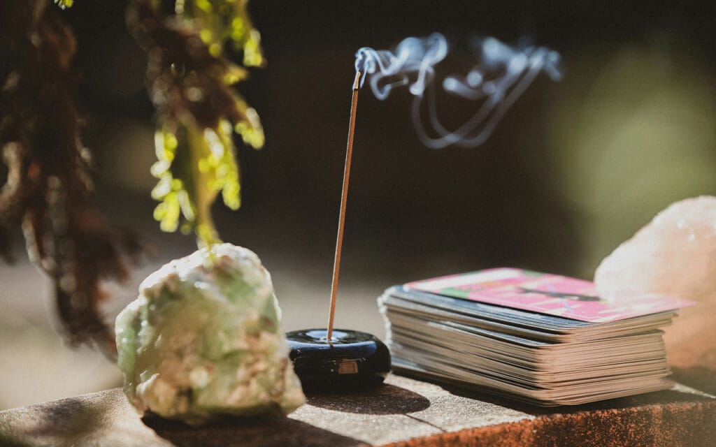 Symbolising slow living, a lit incense stick in a holder sitting between a rock and a deck of cards